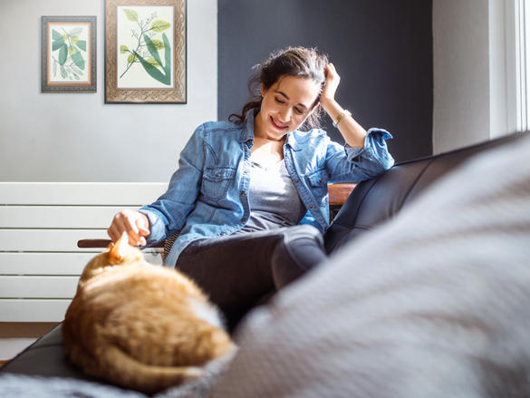 Beautiful young woman relaxing on sofa with her cat in living room.