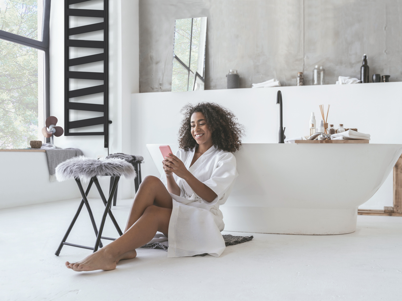 Zehnder_RAD_Ribbon-EL_zeh-nih-keyvisual-300dpi-cmyk Smiling woman sitting in the bathroom on the floor with a smartphone in her hands